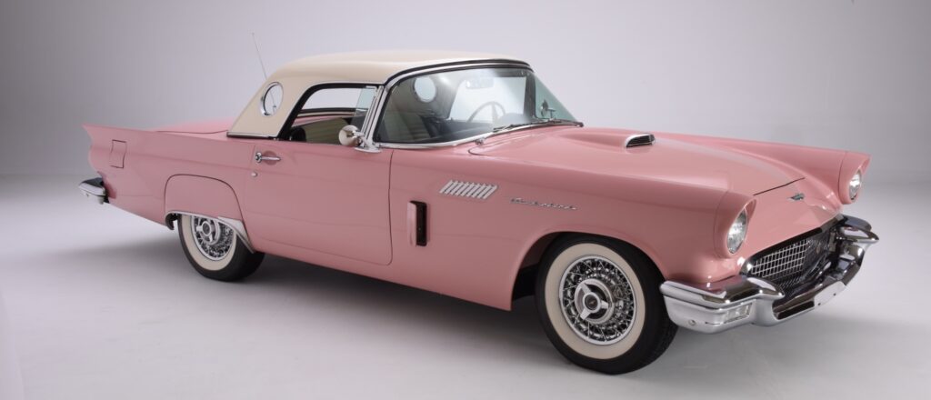 Classic pink convertible car with whitewall tires and beige soft top.