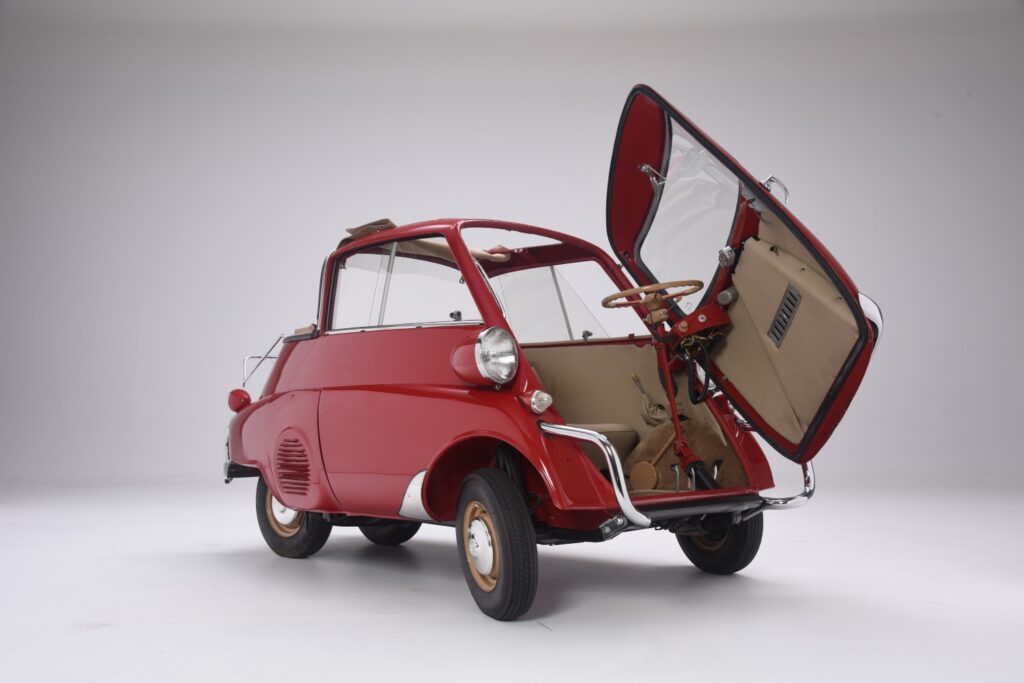 Red vintage microcar with open rear door and beige interior.