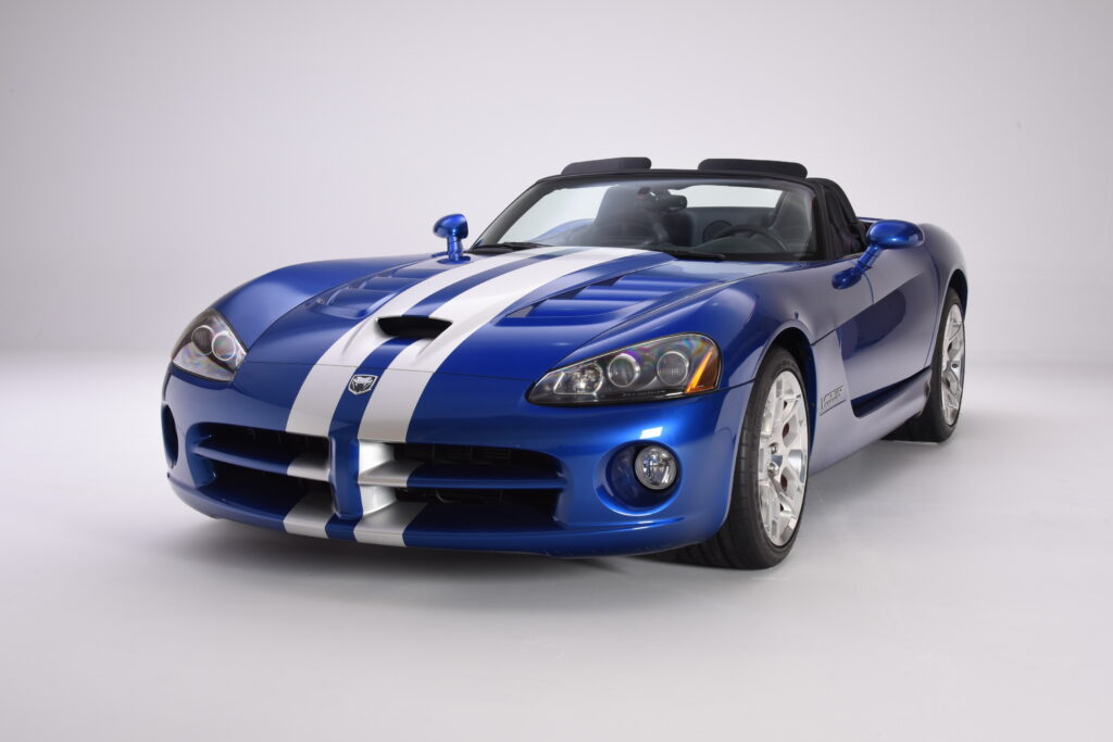 Blue sports car with white racing stripes, convertible top down.