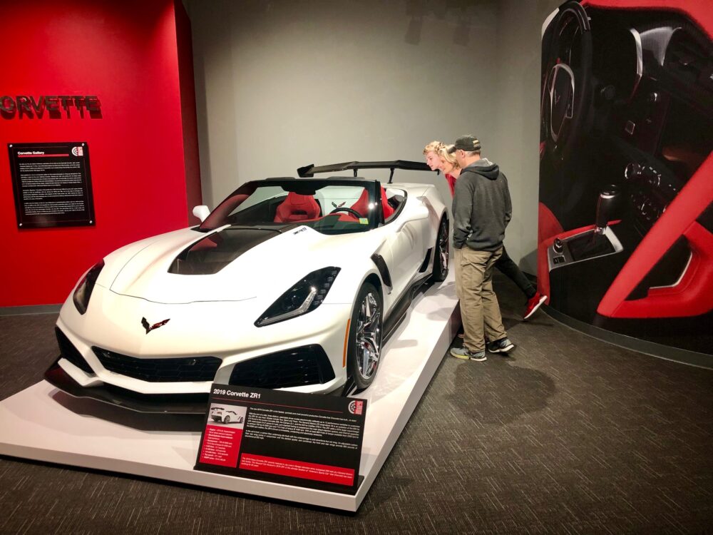 Person admiring a white Corvette sports car on display.