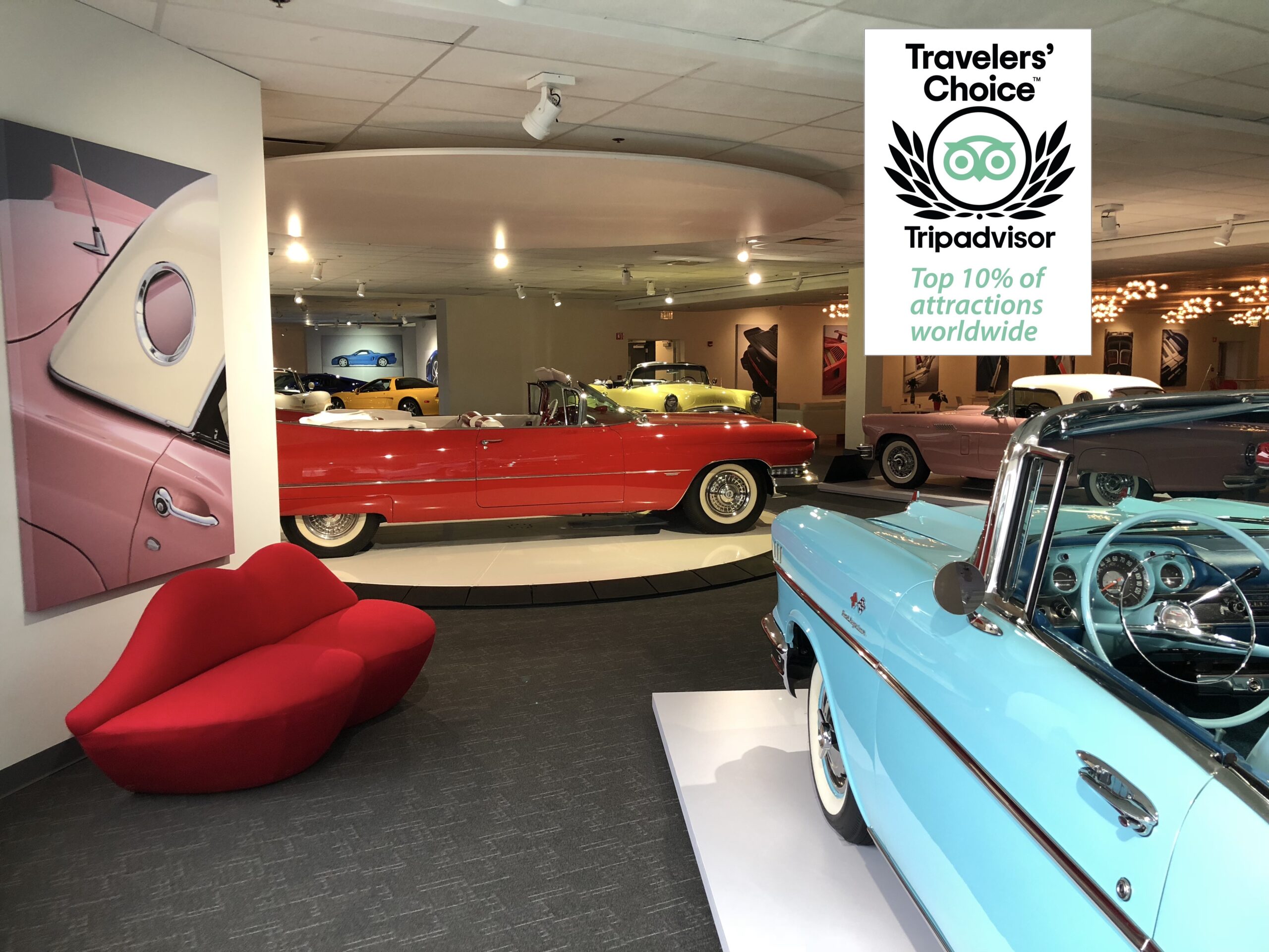 Classic red convertible and blue vintage car displayed indoors with TripAdvisor Travelers' Choice award.