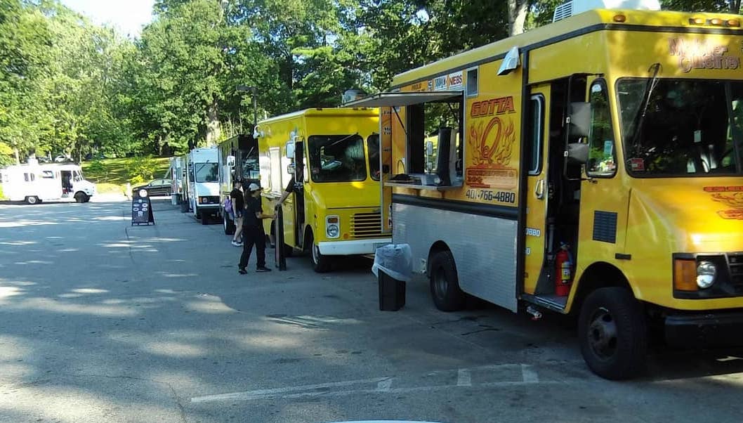 Food trucks lined up on a sunny street with people ordering.