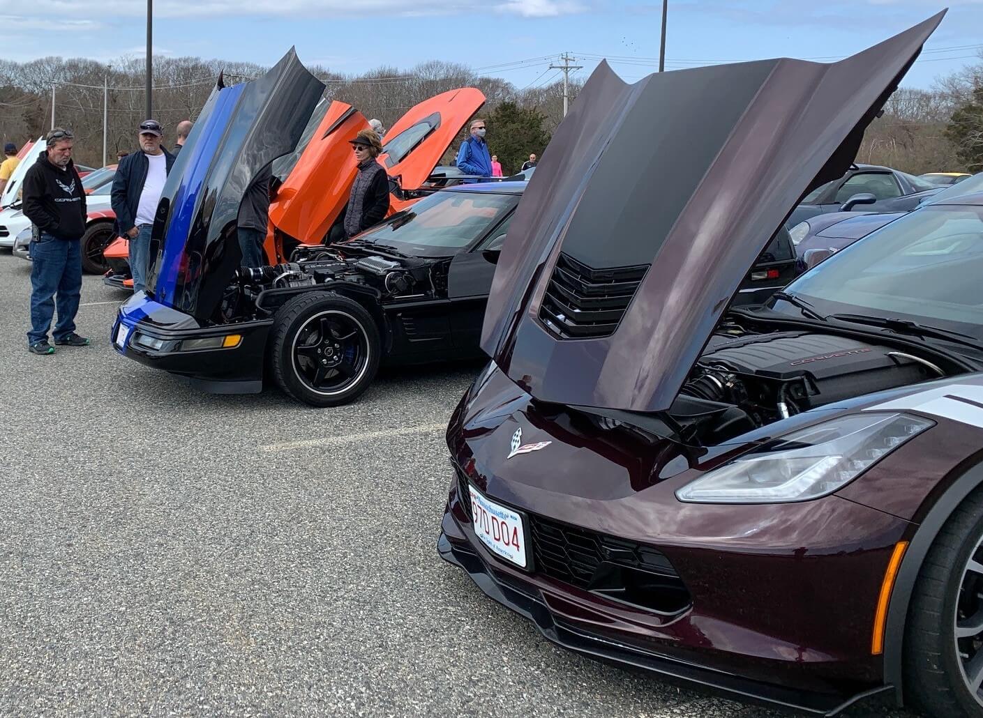 Two sports cars with open hoods at a car event under a clear sky.