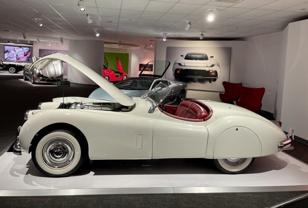 Vintage white convertible classic car with red interior on display.