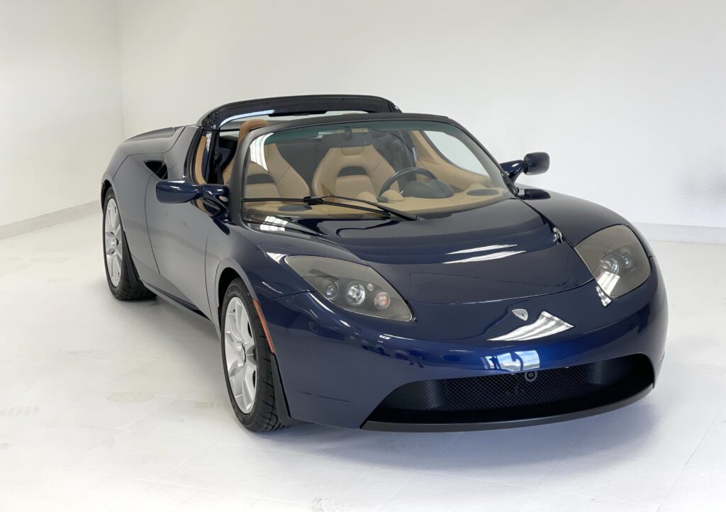 Sleek dark blue Tesla Roadster convertible with a beige interior.