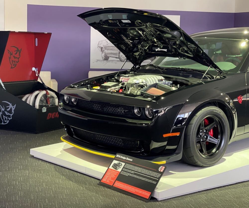 A black Dodge Challenger with its hood open at a car show.