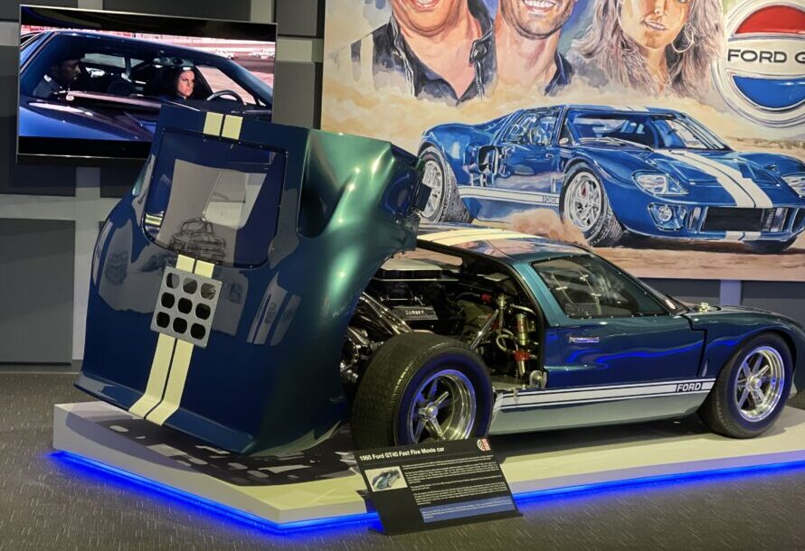 A futuristic, green and blue concept car with its hood open, displayed indoors.