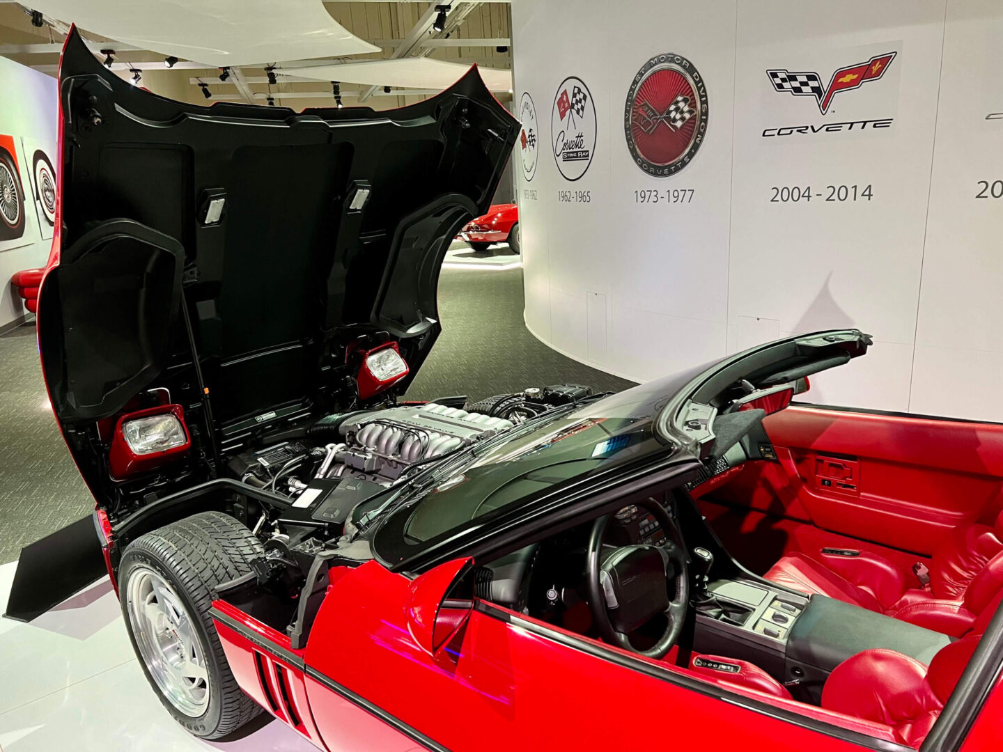 A red convertible sports car with its hood and doors open indoors.