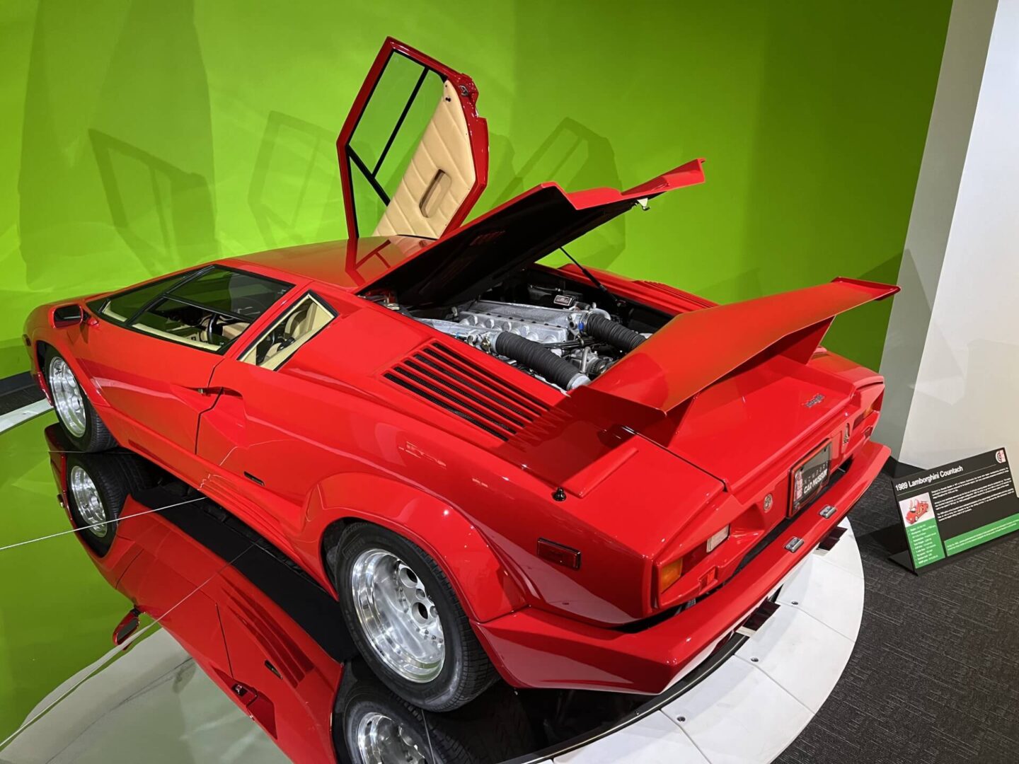 Red sports car with open engine and doors displayed indoors.