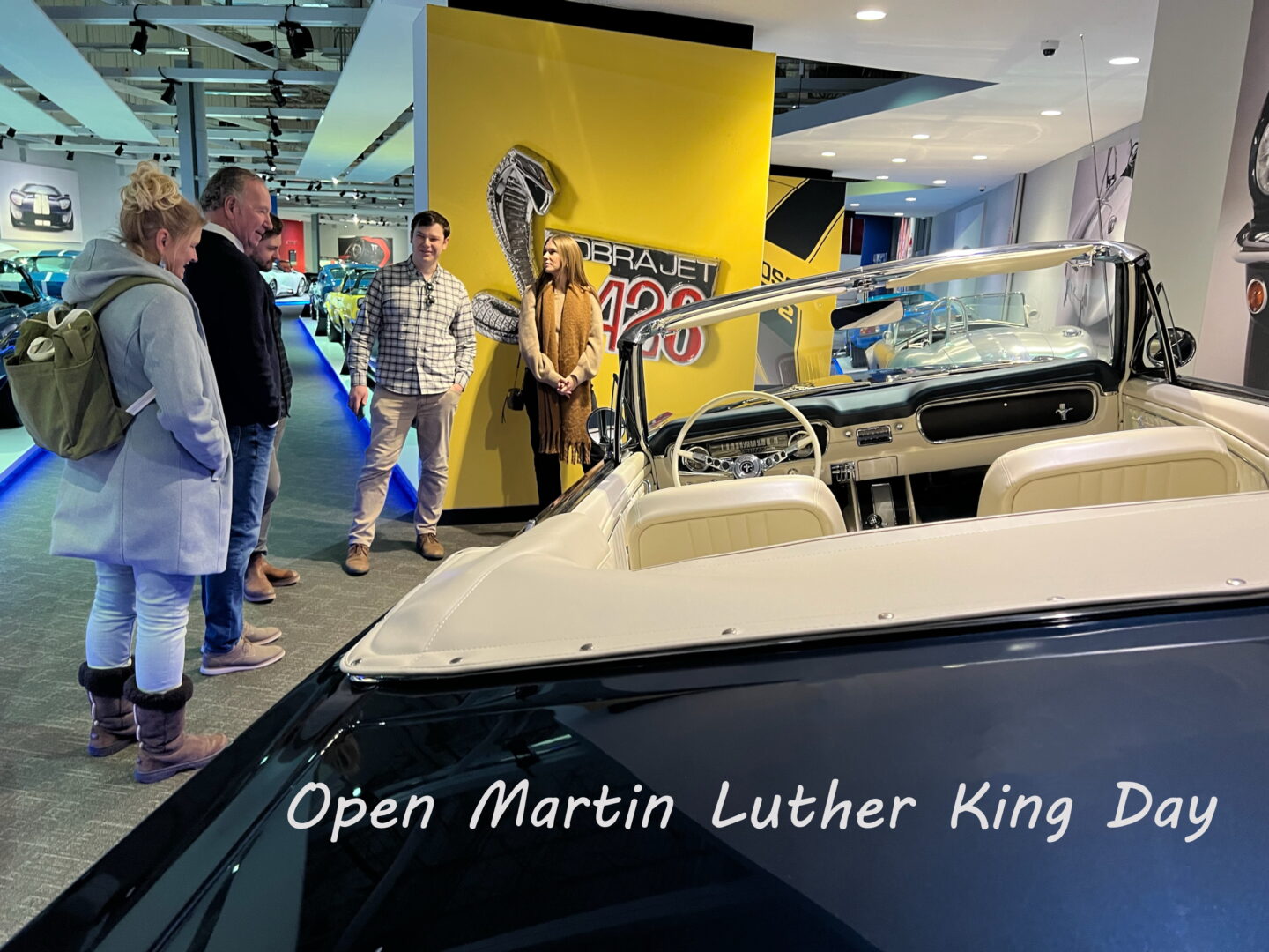 Classic convertible car displayed indoors with people around.