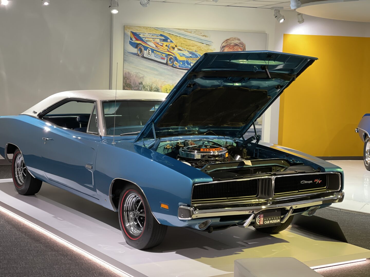 Classic blue muscle car with hood open in a showroom.