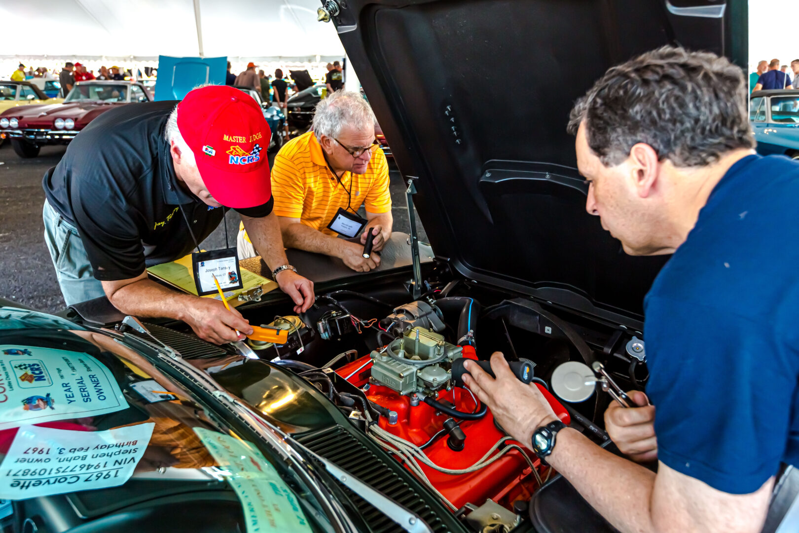 Three men working on a car engine at a car event.